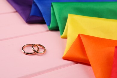 Photo of Rainbow LGBT flag and wedding rings on pink wooden table, closeup
