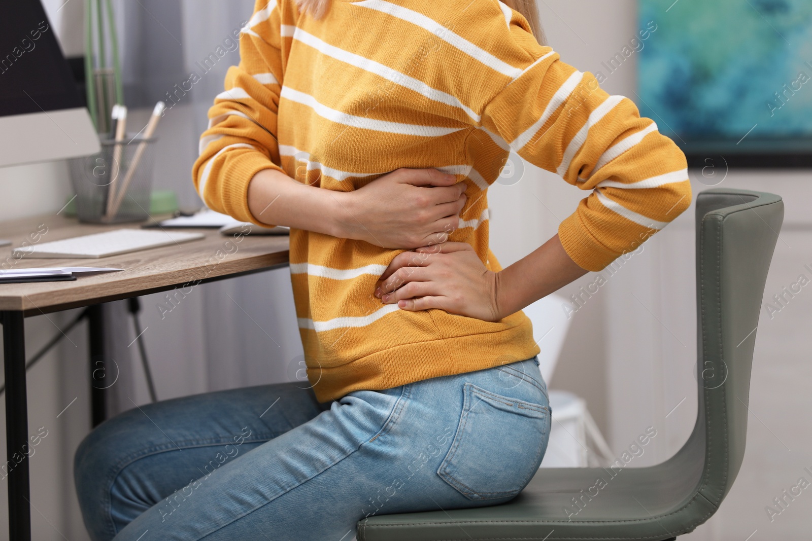 Photo of Young woman suffering from back pain in office, closeup