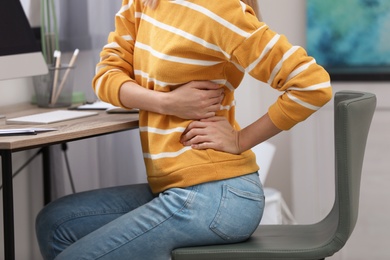 Photo of Young woman suffering from back pain in office, closeup