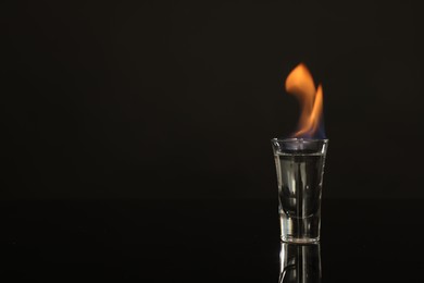 Flaming vodka in shot glass on black background, space for text