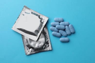 Photo of Pills and condoms on light blue background, flat lay. Potency problem