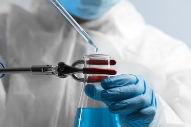 Scientist dripping liquid from pipette into beaker on grey background, closeup