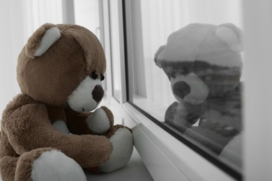 Photo of Cute lonely teddy bear on windowsill indoors, closeup. Space for text