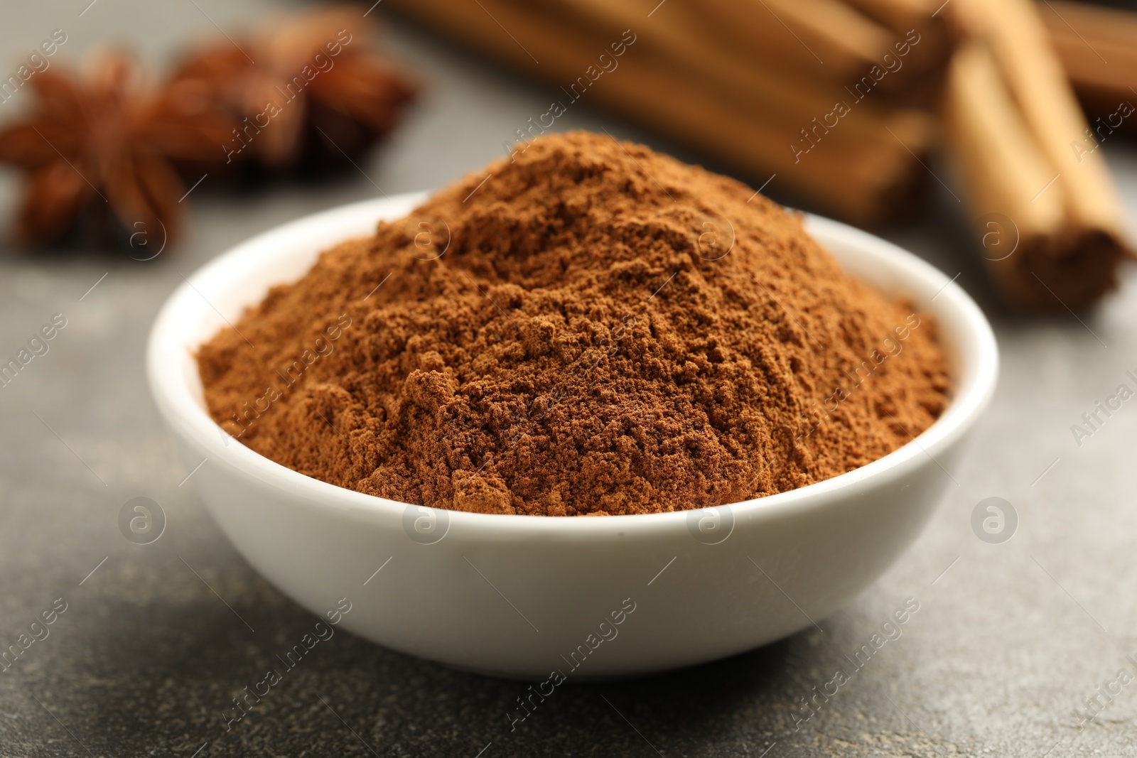 Photo of Bowl of cinnamon powder on grey table, closeup