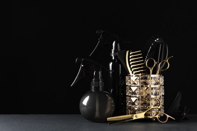 Photo of Different hairdresser tools on grey table against black background. Space for text
