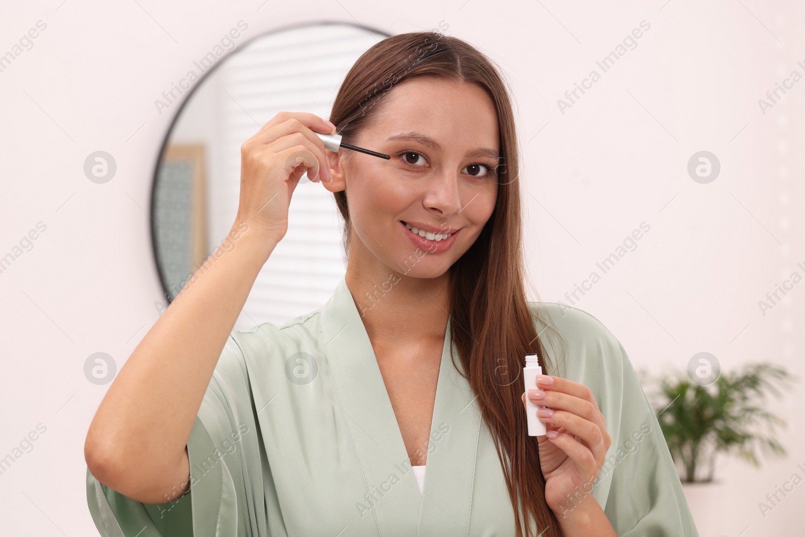 Photo of Beautiful woman applying serum onto eyelashes indoors