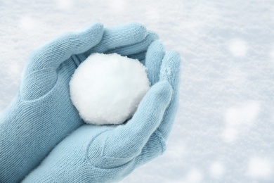 Photo of Woman in light blue gloves holding snowball, closeup