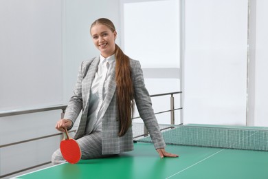 Business woman with tennis racket near ping pong table in office. Space for text
