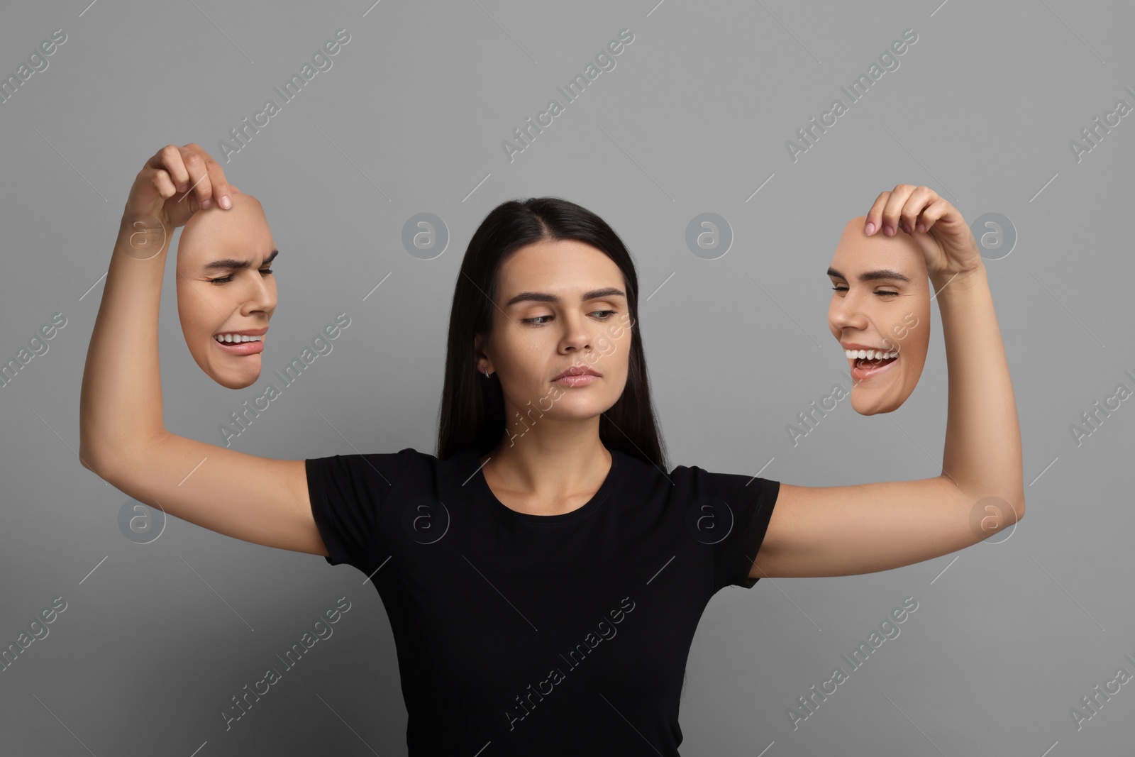 Image of Woman holding masks with her face showing different emotions on grey background. Balanced personality