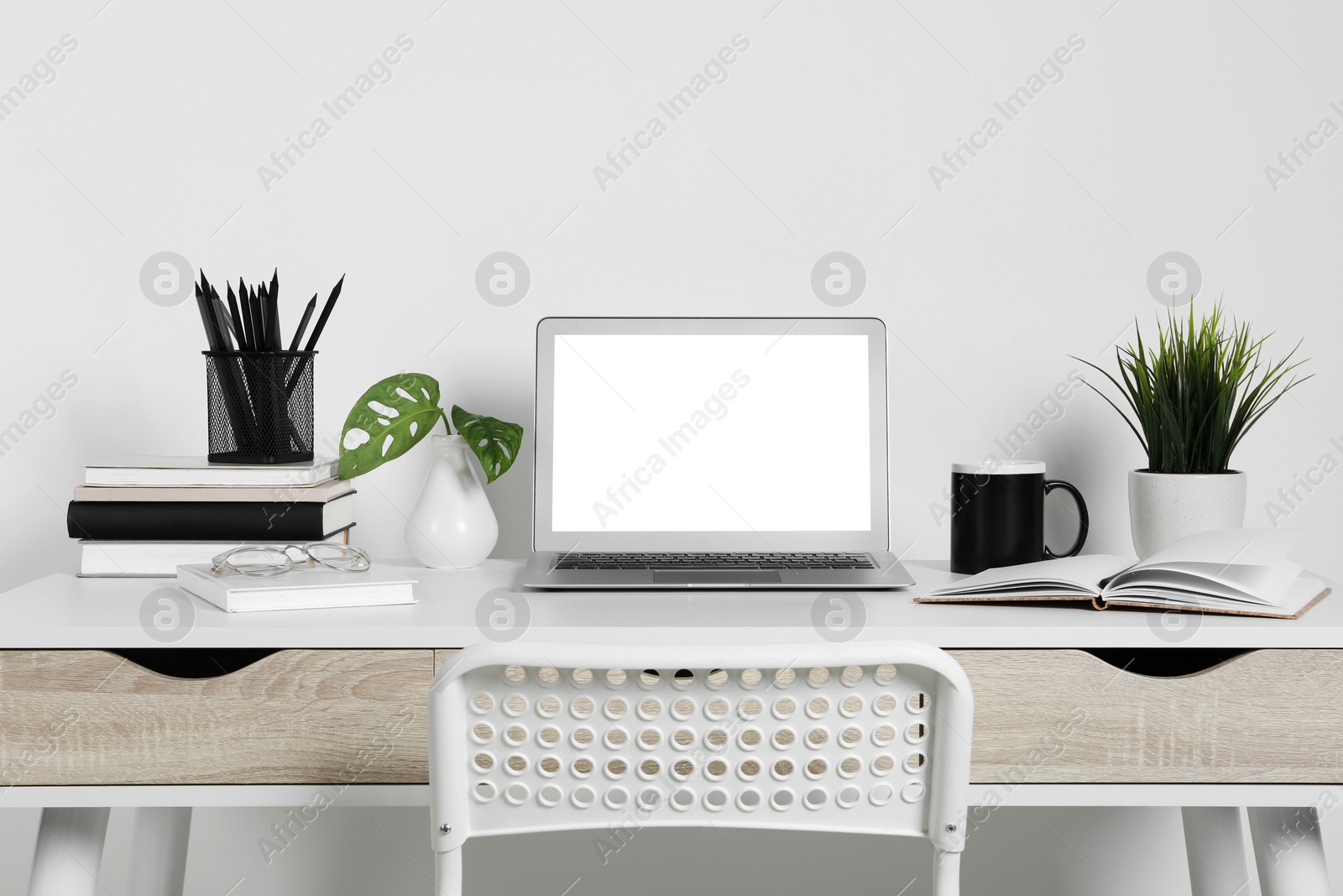 Photo of Cozy workspace with laptop, houseplants and stationery on wooden desk at home