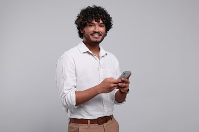 Photo of Handsome smiling man using smartphone on light grey background