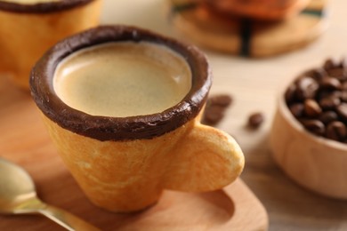 Photo of Delicious edible biscuit cup with espresso and board on table, closeup