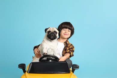 Little boy with his dog in toy car on light blue background