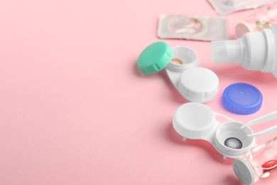 Photo of Cases with color contact lenses, bottle of solution and tweezers on pink background, space for text