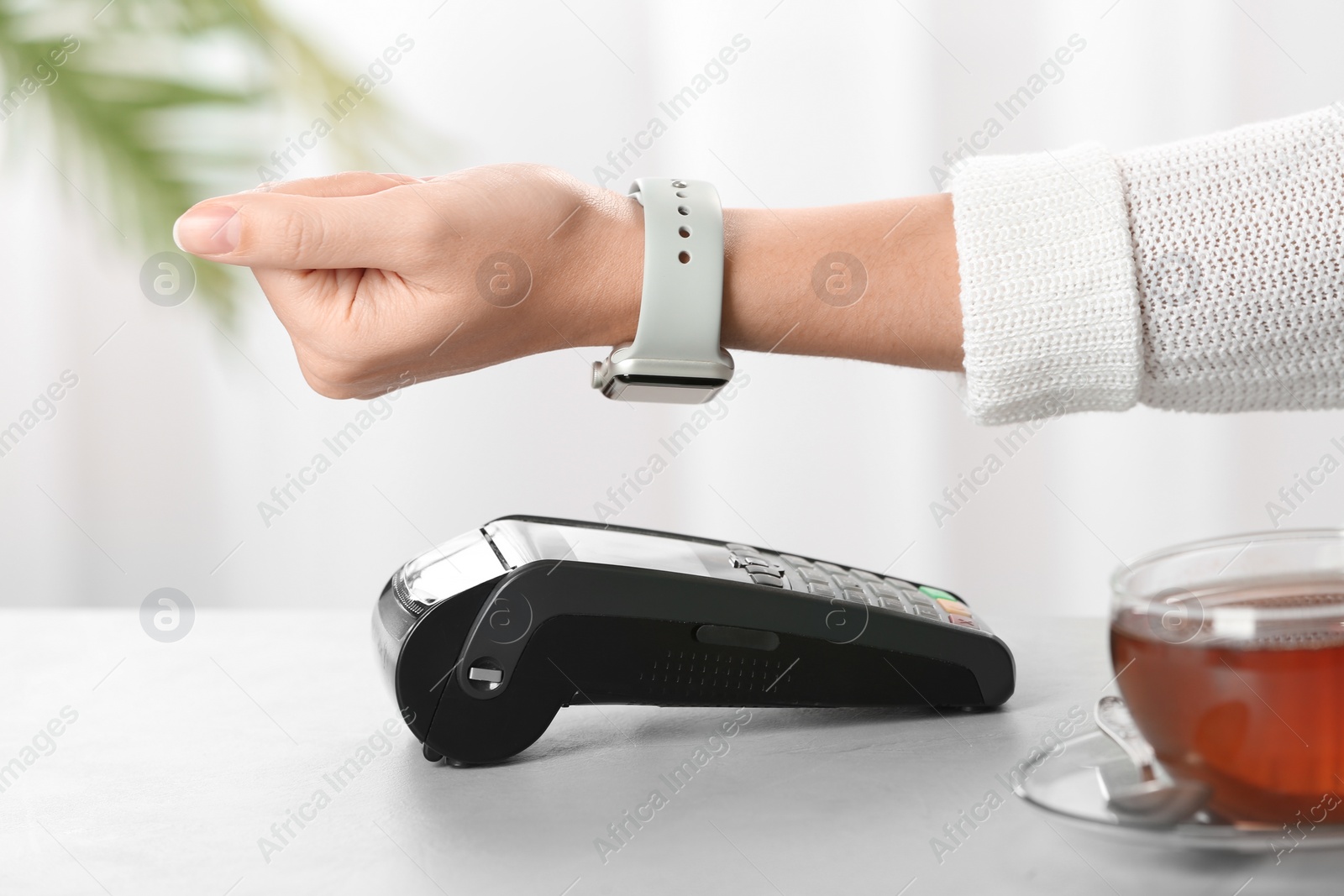 Photo of Woman using terminal for contactless payment with smart watch at table, closeup