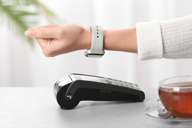 Woman using terminal for contactless payment with smart watch at table, closeup