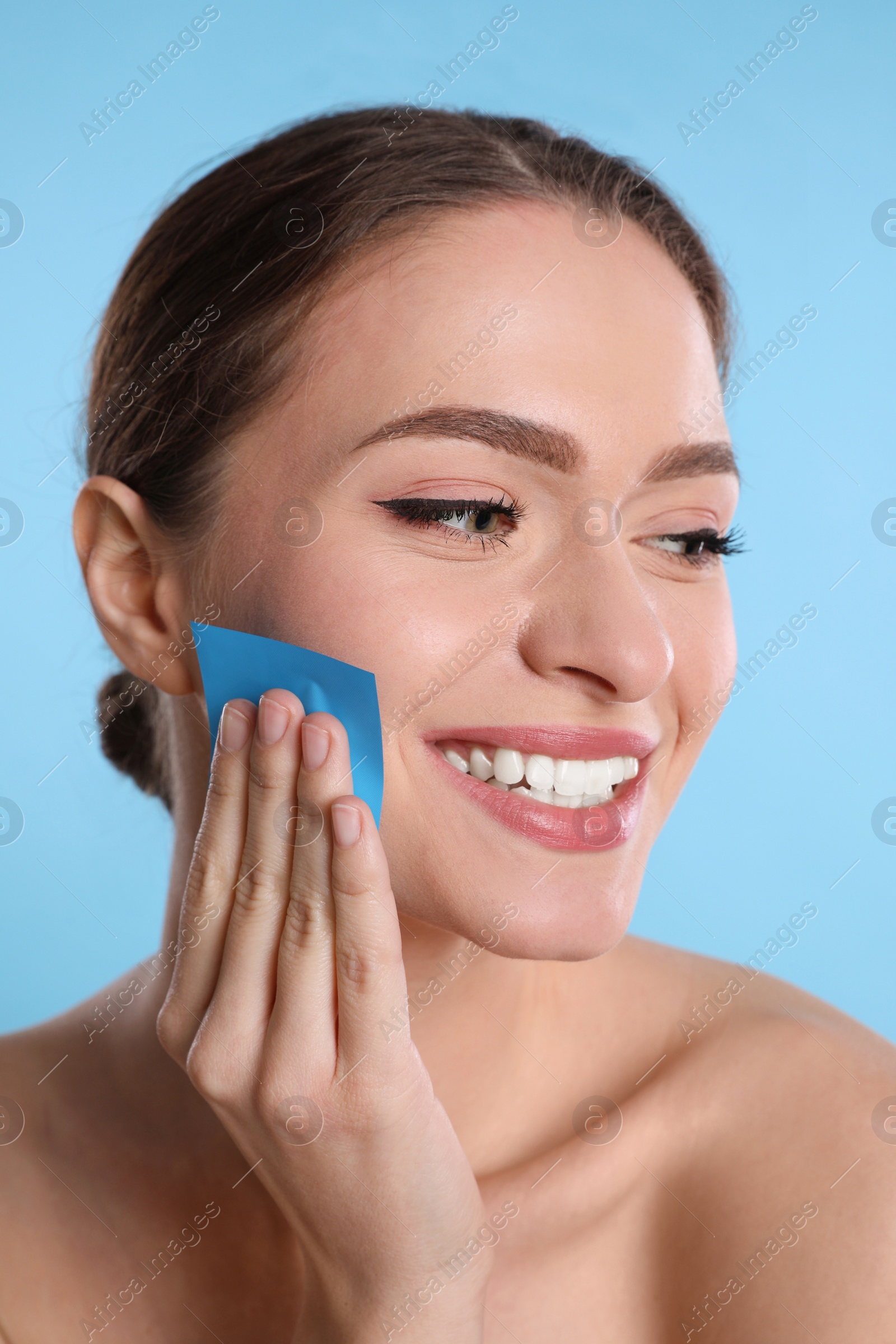 Photo of Beautiful woman using mattifying wipe on light blue background