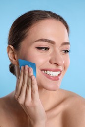 Beautiful woman using mattifying wipe on light blue background