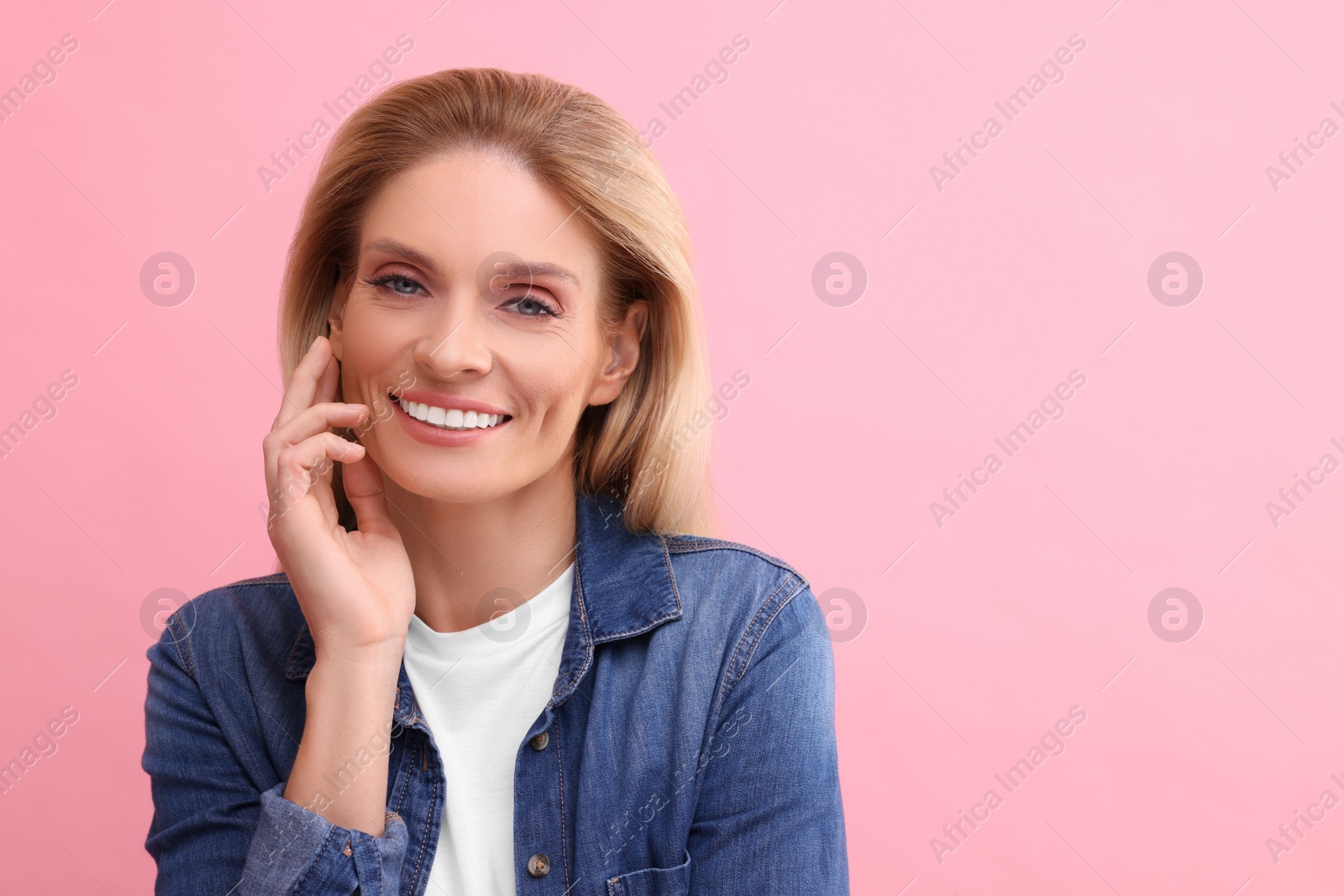 Photo of Portrait of smiling middle aged woman with blonde hair on pink background. Space for text