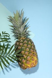 Photo of Whole ripe pineapple and green leaves on light blue background, flat lay