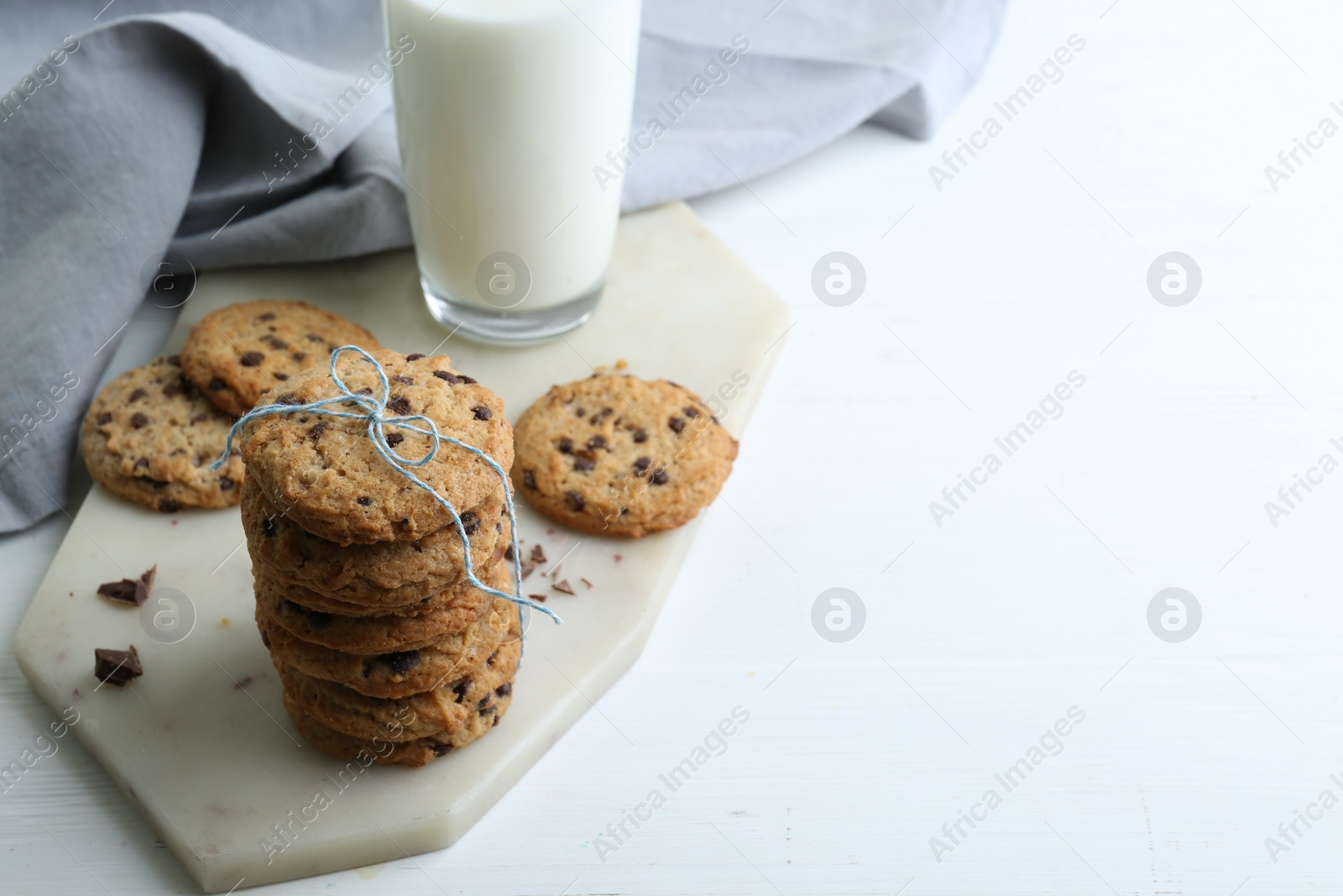 Photo of Tasty chocolate chip cookies and glass of milk on white wooden table. Space for text