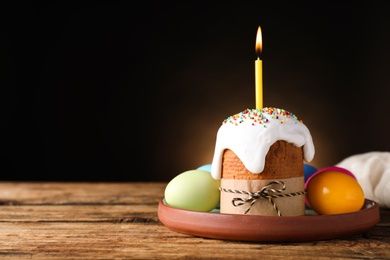 Photo of Traditional Easter cake with burning candle on wooden table against black background. Space for text