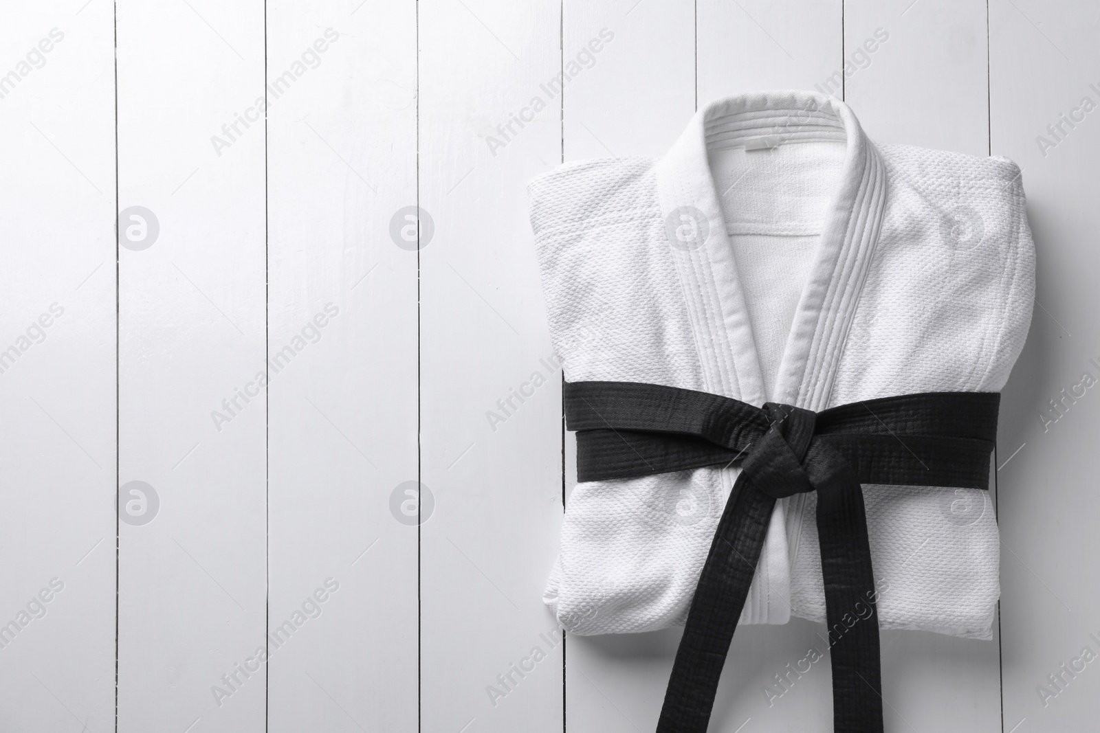 Photo of Martial arts uniform with black belt on white wooden background, top view. Space for text