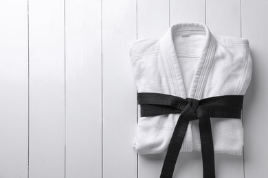 Martial arts uniform with black belt on white wooden background, top view. Space for text