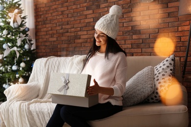 Photo of Beautiful young woman in hat opening gift box at home. Christmas celebration