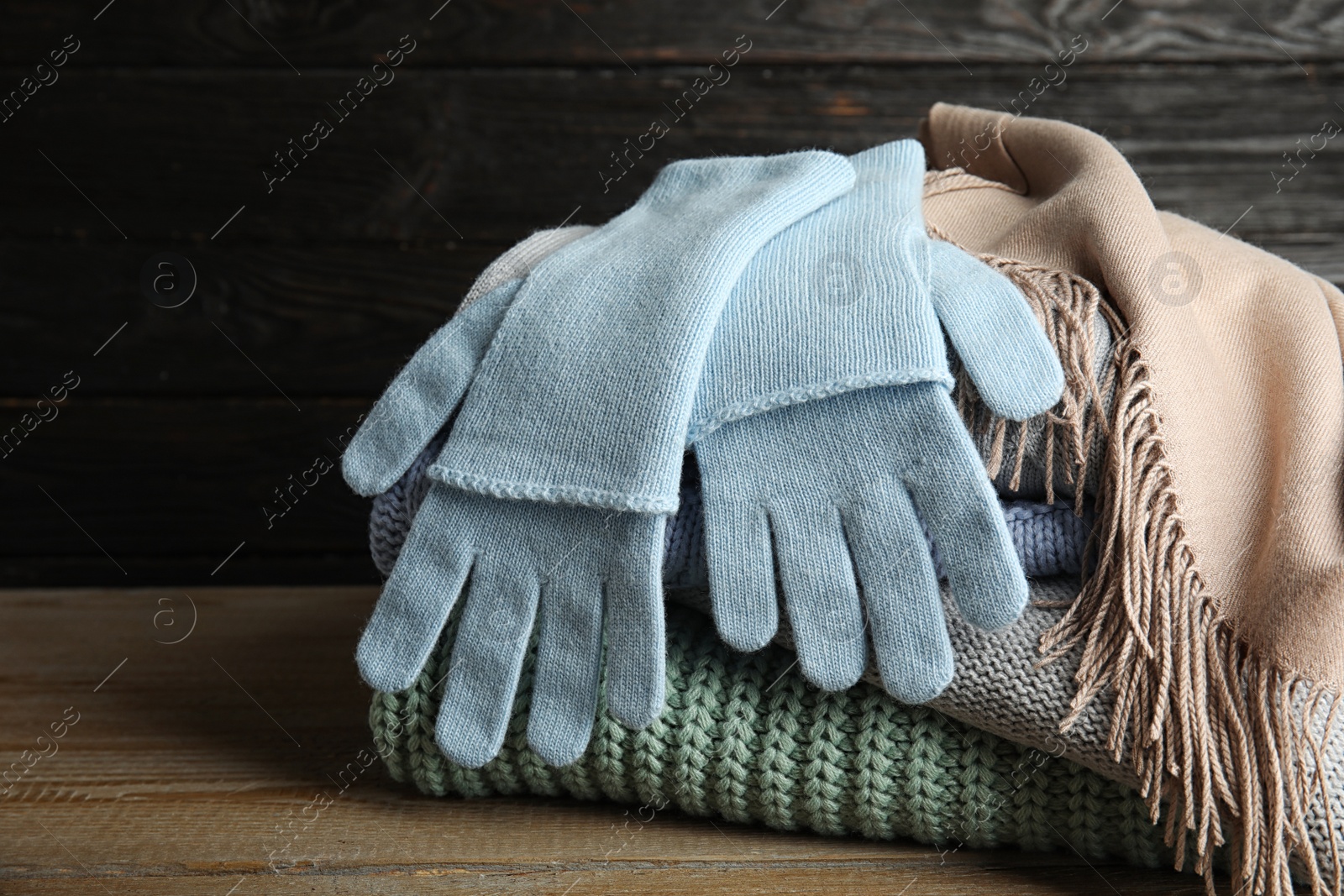 Photo of Stacked sweaters and gloves on wooden table, closeup. Autumn clothes