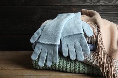 Photo of Stacked sweaters and gloves on wooden table, closeup. Autumn clothes