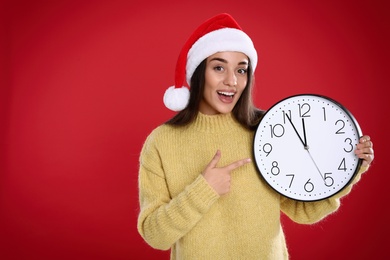 Woman in Santa hat with clock on red background, space for text. New Year countdown