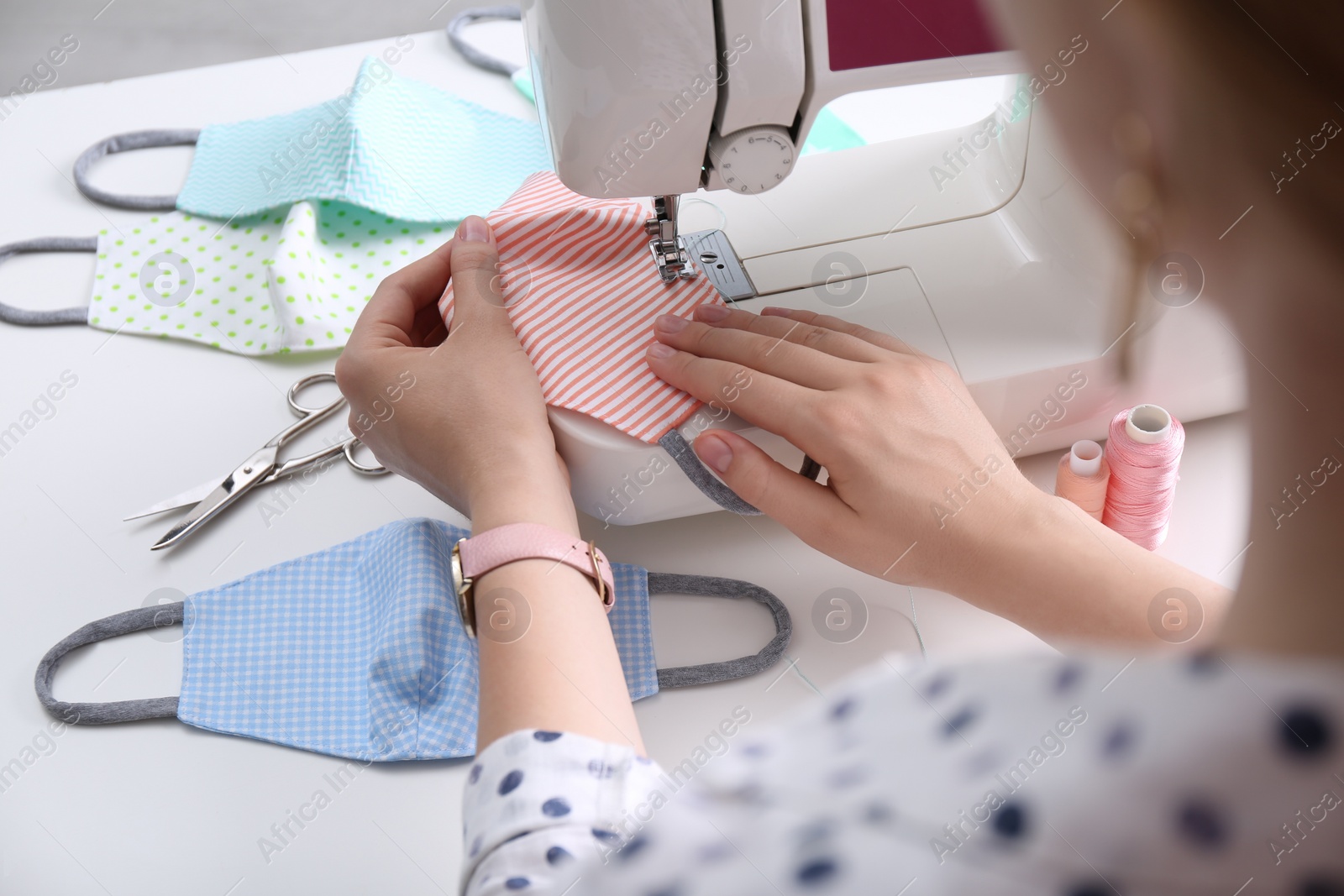 Photo of Woman making cloth mask with sewing machine at white table, closeup