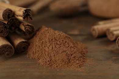 Photo of Aromatic cinnamon sticks and powder on wooden table, closeup