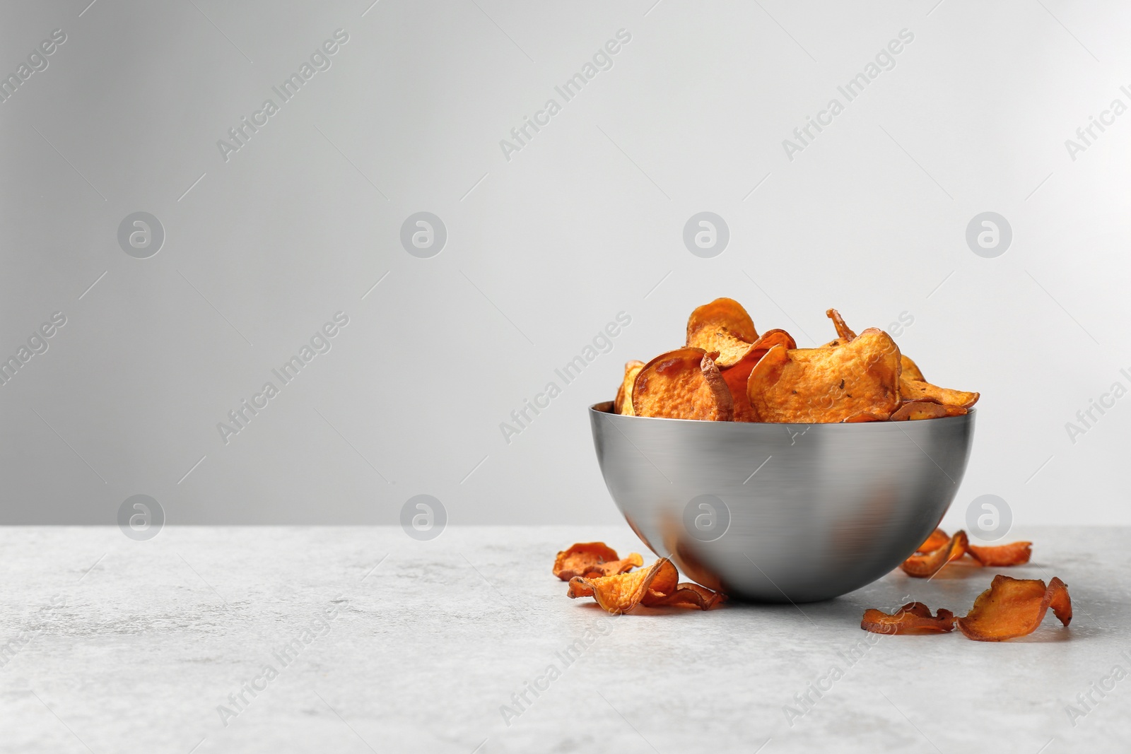 Photo of Bowl and sweet potato chips on table against light background. Space for text