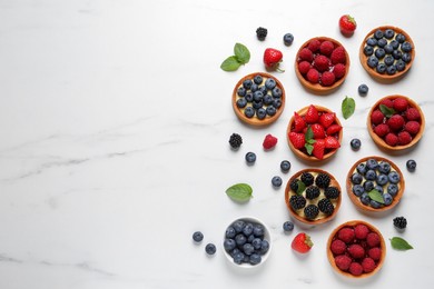 Photo of Tartlets with different fresh berries on white marble table, flat lay and space for text. Delicious dessert