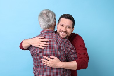 Photo of Happy son and his dad hugging on light blue background