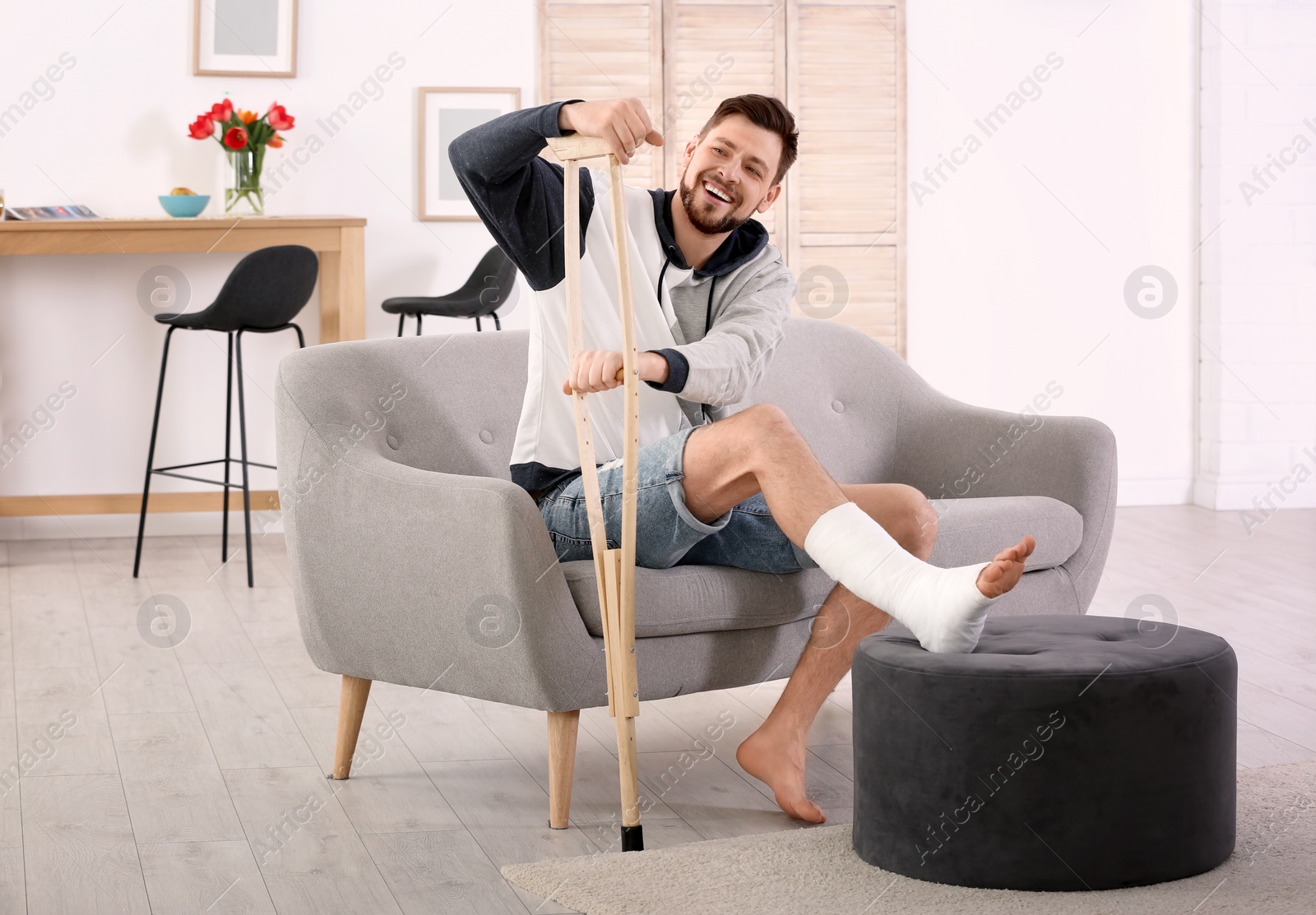 Photo of Mature man with crutch and broken leg in cast sitting on sofa at home