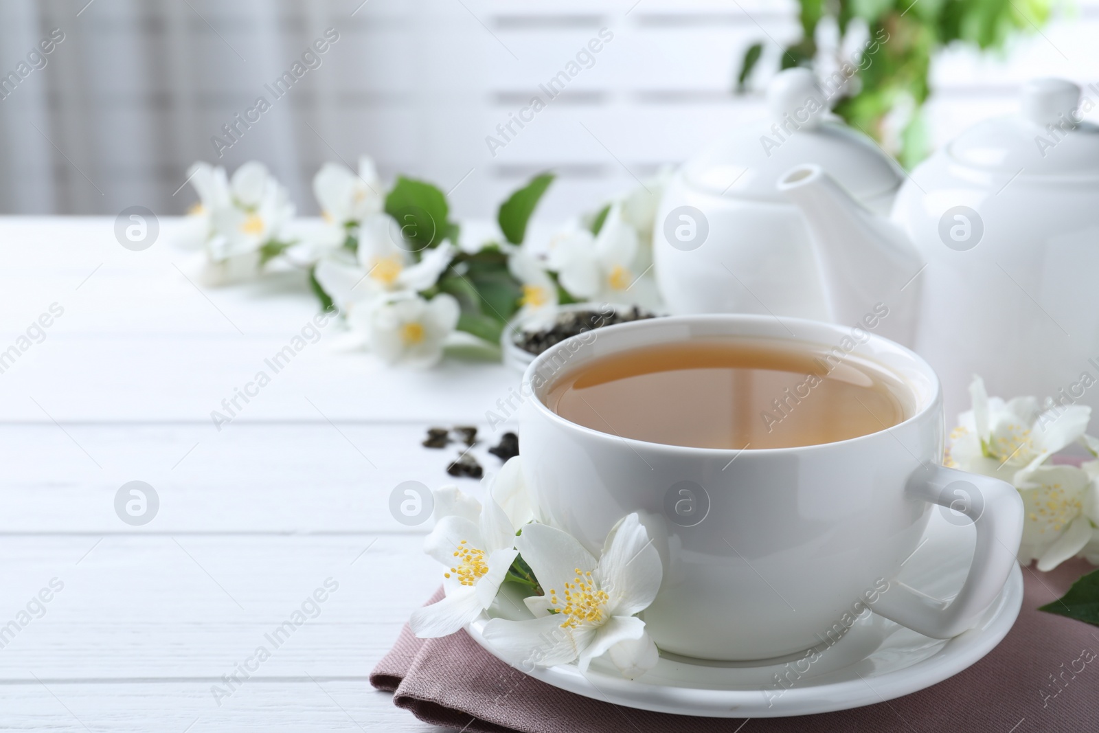 Photo of Cup of tea and fresh jasmine flowers on white wooden table. Space for text