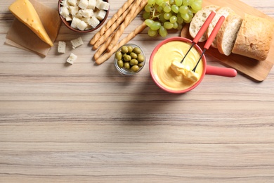 Photo of Flat lay composition with pot of cheese fondue and products on wooden table, space for text