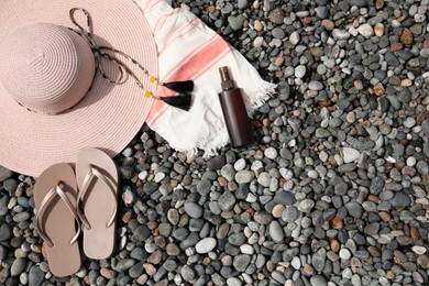 Beautiful hat, sunscreen and flip flops on pebbles, flat lay. Space for text