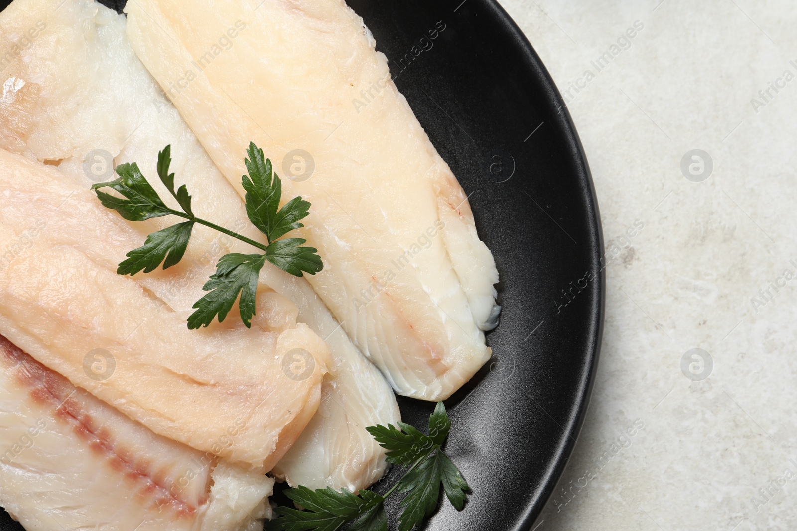 Photo of Plate with raw cod fish and parsley on light textured table, top view