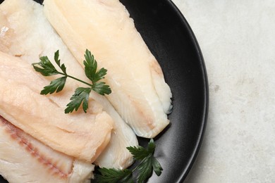 Plate with raw cod fish and parsley on light textured table, top view