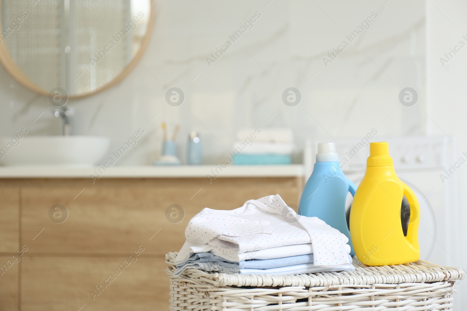 Photo of Bottles of detergent and children's clothes on wicker basket in bathroom. Space for text