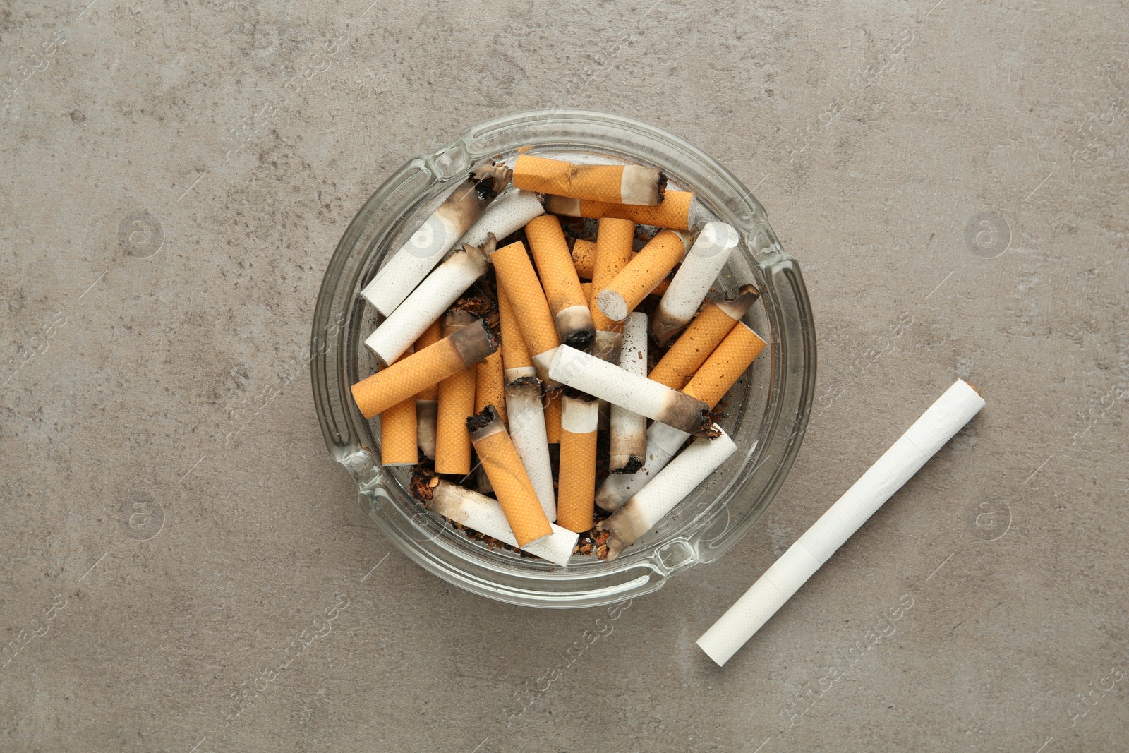 Photo of Glass ashtray with cigarette stubs on grey table, flat lay