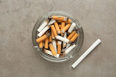 Glass ashtray with cigarette stubs on grey table, flat lay