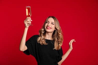 Happy young woman with glass of champagne on red background. Christmas celebration