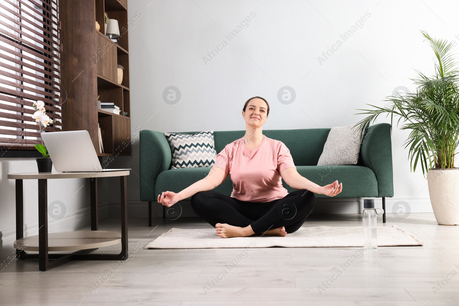 Photo of Overweight woman meditating on rug at home