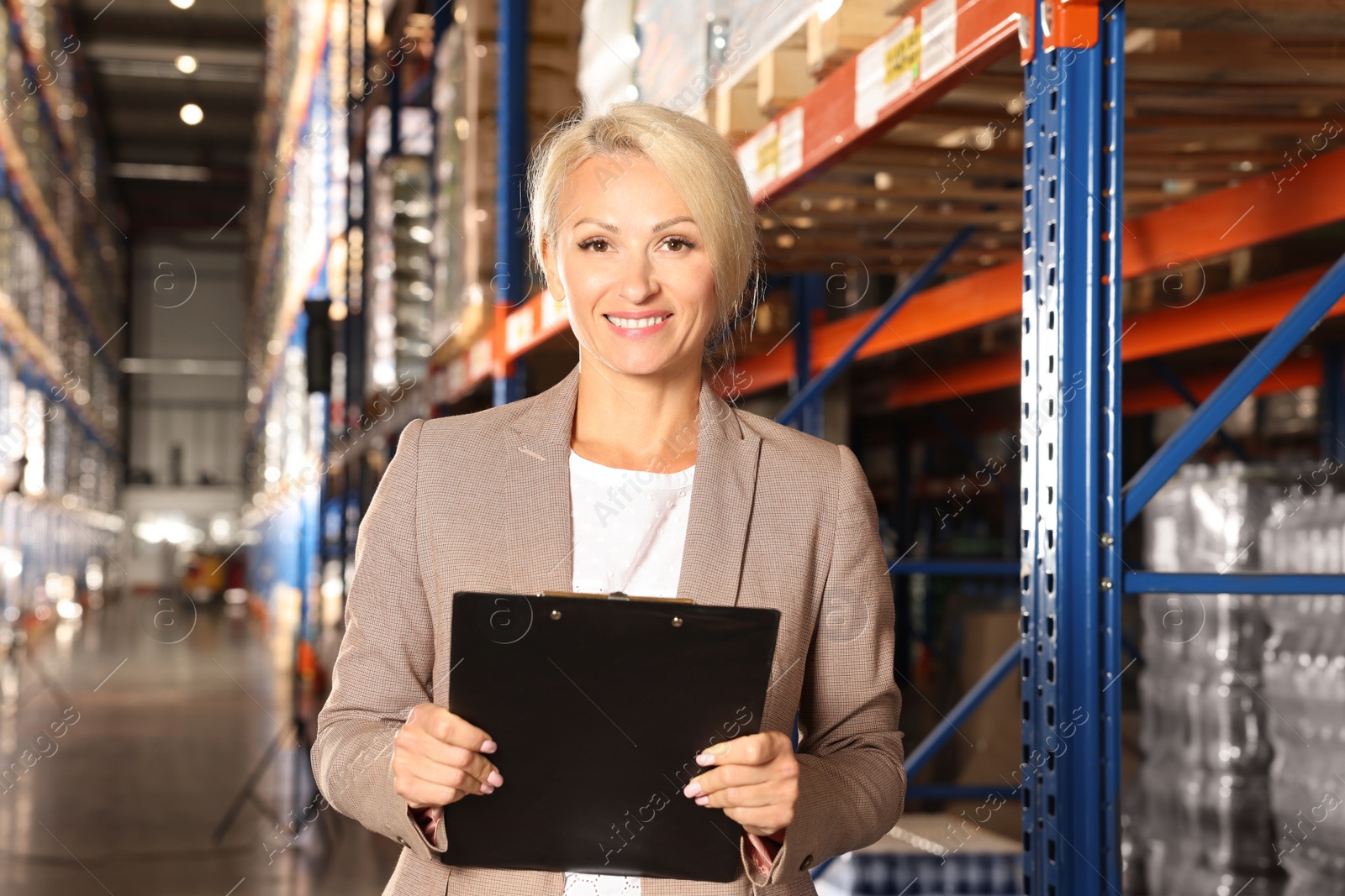 Photo of Happy manager holding clipboard in warehouse with lots of products