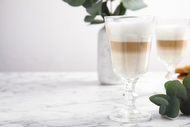 Delicious latte macchiato and eucalyptus branch on white marble table. Space for text
